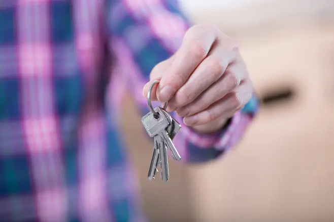 A man’s hand in a purple checked shirt holding the keys to his flat